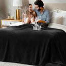 Man and woman sitting on a bed with a black blanket and a glass of water being poured over it.