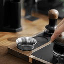 Coffee brewing setup with a metal filter and wooden plunger on a wooden surface.