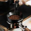 Hand using a magnetic ring and a  coffee distribution tool on coffee grounds 